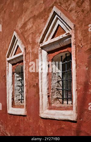 Due finestre con gabbia metallica in fila sul muro di un vecchio edificio rosso. Antico edificio in pietra. Semplice cornice decorativa intorno alla finestra. Foto Stock