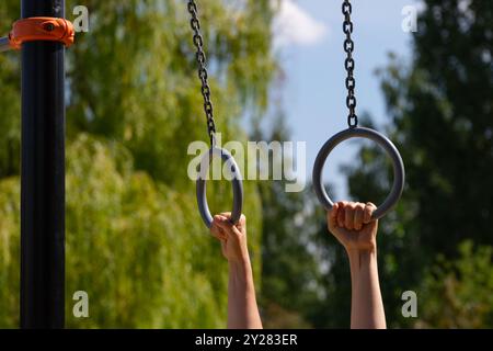 La persona tiene le mani sugli anelli da ginnastica all'aperto. Foto Stock