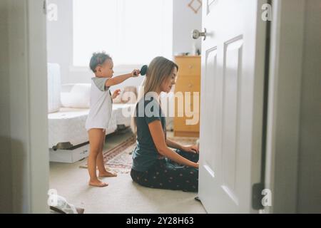 Una bambina che si pulisce i capelli della madre a casa. Foto Stock