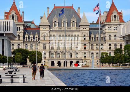 Persone che camminano di fronte all'edificio del Campidoglio dello Stato di New York ad Albany, New York, accanto alla piscina riflettente dell'Empire State Plaza Foto Stock