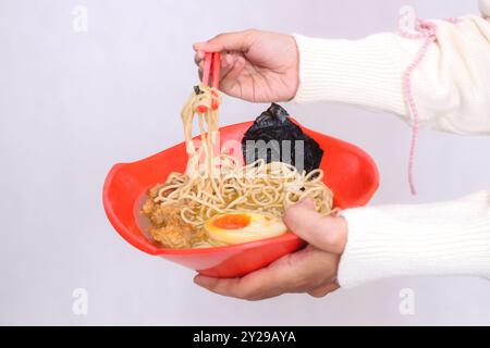 mano di donna asiatica in hijab che trasporta ciotola di ramen (cibo cinese) e raccoglie spaghetti con bacchette per pubblicità, cibo e contenuti culinari Foto Stock