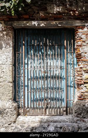 Primo piano di una finestra a reticolo chiusa da una tapparella di legno blu in luce e ombra, incorniciata da pietra e mattoni nella città vecchia, Cartagena, Colombia, Sud Foto Stock