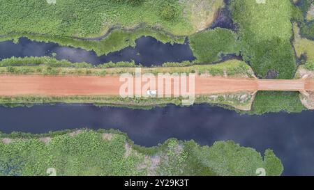 Vista aerea verticale lungo la strada sterrata della Transpantaneira con un'auto e le adiacenti lagune blu e prati verdi, paludi, Mato grosso, Brasile, Sud A. Foto Stock