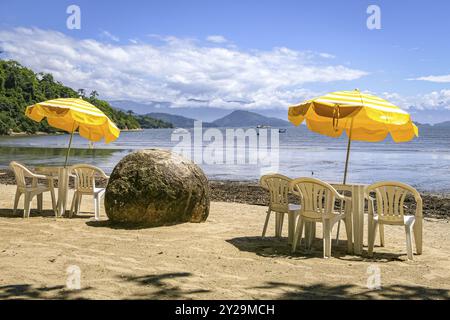 Spiaggia con tavolo, sedie, ombrelloni gialli, masso di granito e splendida vista sul mare, parati, Brasile, Sud America Foto Stock