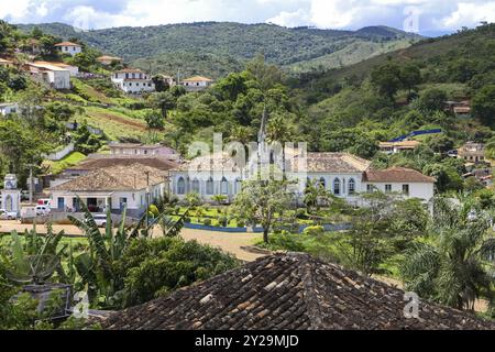 Vista in una valle con edifici coloniali e montagne ricoperte di lussureggiante foresta atlantica a Serro, Minas Gerais, Brasile, Sud America Foto Stock