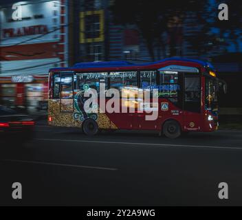 Balikpapan, Indonesia - 9 agosto 2024. Un autobus Balikpapan City Trans attraversa una vivace strada urbana di notte, illuminata dalle luci della città e. Foto Stock
