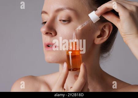 Donna che applica un contagocce di siero facciale sulla pelle dimostrando la cura della pelle e il trattamento di bellezza. concetto di cura della pelle del viso e rimedio per le rughe, agina della pelle Foto Stock