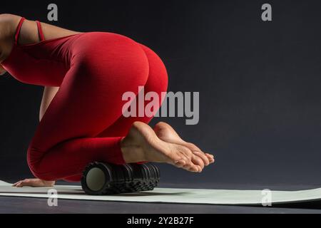 Donna sportiva che fa un massaggio corpo con rullo in schiuma su fondo nero. Rilassamento muscolare. Concetto di stile di vita sportivo, bellezza, corpo e salute, Foto Stock
