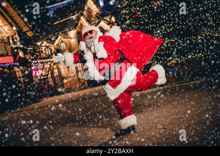 Full size ritratto di overjoyed funky Santa Hold età presenta sacco divertirsi buon umore christmastime decorazione luci all'aperto Foto Stock