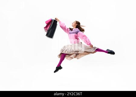 Saltando attraverso l'aria con borse in mano, la giovane donna sfoggia il suo elegante e luminoso outfit su sfondo bianco studio. Foto Stock