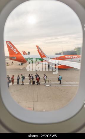 Persone in coda per salire a bordo di un volo Easyjet sulla pista scattata dal finestrino dell'oblò della cabina Foto Stock