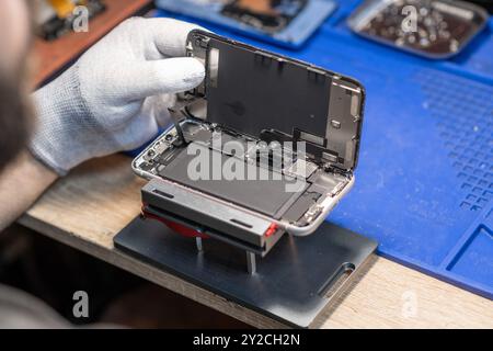 Un tecnico sostituisce accuratamente la batteria di uno smartphone mentre lavora in un'officina di riparazione tecnica ben attrezzata Foto Stock