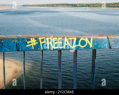 Zaporizhzhia, Ucraina - 20 agosto 2024: Hashtag #FREEAZOV (libertà per i soldati ucraini dell'unità Azov) sulla recinzione del molo sullo sfondo Foto Stock