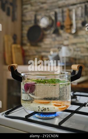 Le verdure bollono in una pentola trasparente d'acqua su una stufa a gas Foto Stock