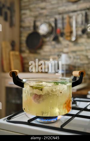 Cuocere gnocchi di carne in brodo vegetale bollente in una pentola trasparente su un piano cottura a gas Foto Stock