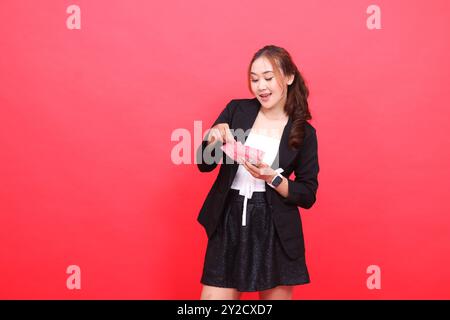 gesto di una giovane donna d'ufficio indonesiana, allegra e sincera, che indossa una tuta formale nera contante i soldi della rupia, per contenuti finanziari, affari, pubblicità, Foto Stock