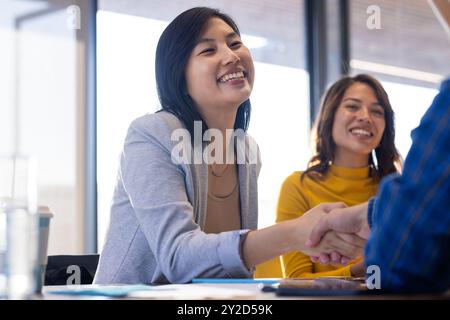 Donna d'affari asiatica sorridente che stringe la mano durante una riunione in un ufficio moderno Foto Stock