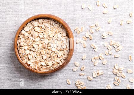 Fiocchi d'avena arrotolati, fiocchi d'avena arrotolati in una ciotola di legno su lino. Le farine d'avena cotte e cotte a vapore sono state arrotolate in fiocchi e leggermente tostate. Foto Stock