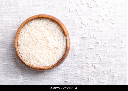 Riso basmati bianco, in una ciotola di legno su tessuto di lino. Chicchi lunghi e sottili con aroma e gusto aromatici. Chicchi di riso di un Oryza sativa. Foto Stock