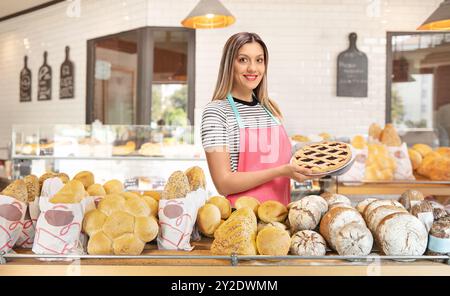 Giovane donna che tiene una torta appena sfornata in una panetteria Foto Stock