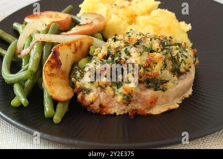 Bistecca di lombo di maiale al forno con crosta di panko alle erbe, fagioli verdi, mele saltate e purè di patate Foto Stock