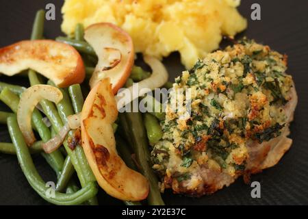 Bistecca di lombo di maiale al forno con crosta di panko alle erbe, fagioli verdi, mele saltate e purè di patate Foto Stock