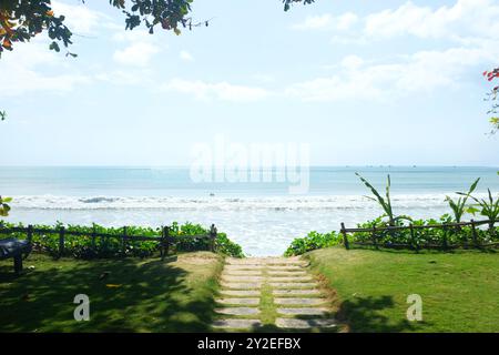 Soleggiato sentiero della spiaggia che conduce all'Oceano, incorniciato da lussureggiante vegetazione e da un limpido cielo blu. Questa invitante scena cattura un affascinante Sentiero in pietra Foto Stock