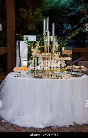 Elegante tavolo da dessert all'aperto con decorazioni a lume di candela e decorazioni floreali. Foto Stock