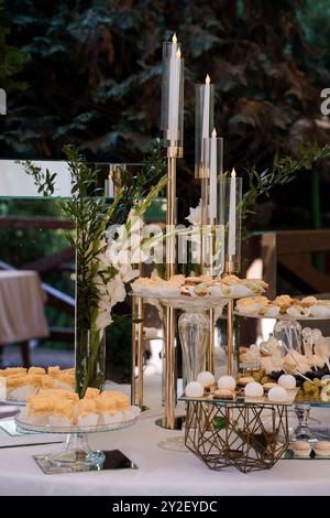 Elegante tavolo da dessert all'aperto con candele e decorazioni floreali per l'evento celebrativo. Foto Stock