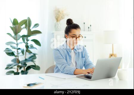 Donna d'affari di etnia araba o indiana, impegnata e concentrata in blu, camicia con occhiali, manager aziendale o seo digitale, seduta sul posto di lavoro utilizza un laptop, concentrata lavora su un nuovo progetto Foto Stock