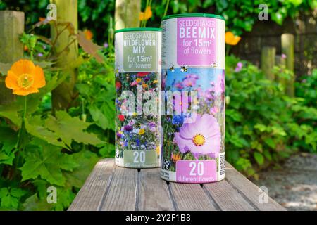 Due lattine di Seedshaker Beemix e Wildflower si mescolano in un giardino con fiori. Le taniche contengono semi diversi per una varietà di fiori Foto Stock