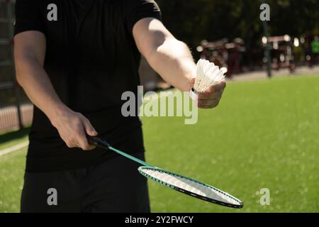 Mans mani con racchetta da badminton e rubinetto sul campo sportivo nelle giornate di sole. All'aperto. Primo piano. Foto Stock