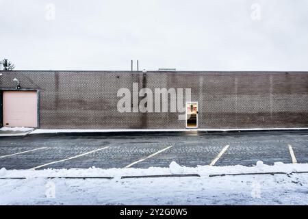 Ontario, Canada, 31DEC 2015 - retro di un edificio in cemento con una sola porta di fronte a un parcheggio vuoto in una giornata invernale innevata Foto Stock