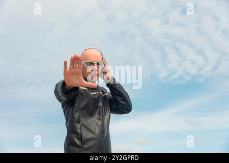 Uomo calvo e attraente con occhiali da sole e cuffie. All'aperto con sfondo blu Foto Stock