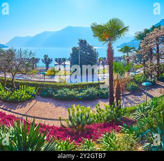 La sorgente Parco Villa Malpensata con palme di chusan, Euphobia fiorita (spurge), Erica Carnea (brughiera di primavera) di fronte al nebbioso Ceresio e alle Alpi, Lugan Foto Stock