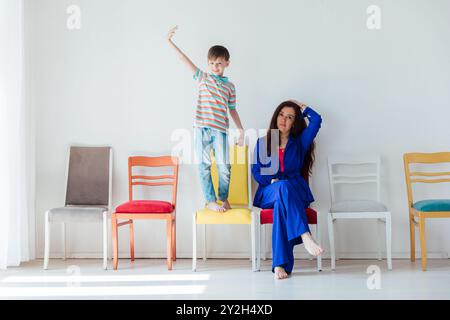 Donna in abito blu e figlio seduto e molte sedie diverse Foto Stock