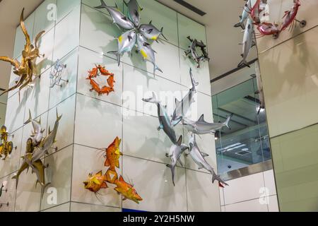 Colorate sculture di pesci metallici con squali e granchi su moderne pareti bianche all'aeroporto di Miami. Foto Stock