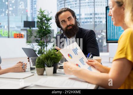 Consulente finanziario in ufficio che fornisce servizi economici ai clienti, mostrando loro grafici. Il consulente parla con i membri della famiglia dei loro conti bancari, dando consigli Foto Stock