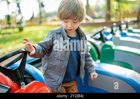 Simpatico bambino che cavalca un'auto giocattolo divertendosi in un parco giochi all'aperto nella calda giornata autunnale. Divertimento attivo per i bambini in autunno. Foto Stock