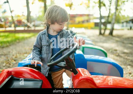Simpatico bambino che cavalca un'auto giocattolo divertendosi in un parco giochi all'aperto nella calda giornata autunnale. Divertimento attivo per i bambini in autunno. Foto Stock
