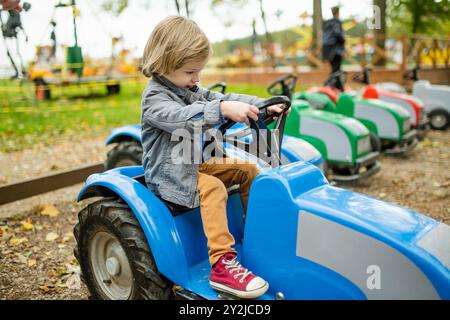 Simpatico bambino che cavalca un'auto giocattolo divertendosi in un parco giochi all'aperto nella calda giornata autunnale. Divertimento attivo per i bambini in autunno. Foto Stock