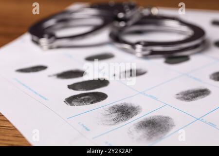 Foglio di carta con impronte e manette umane sul tavolo, primo piano. Condanna penale Foto Stock