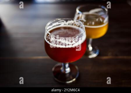 Due bicchieri di birra artigianale sono collocati su un tavolo di legno in un accogliente bar. Un bicchiere contiene ale ambra, mentre l'altro presenta una lager chiara Foto Stock