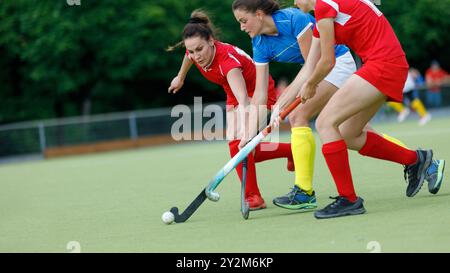 Tre giocatrici competono per la palla durante una partita di hockey su prato. Foto Stock