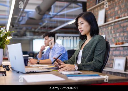 Lavorando in un ufficio moderno, donna asiatica che utilizza un computer portatile e uno stilo per lavori di progettazione Foto Stock