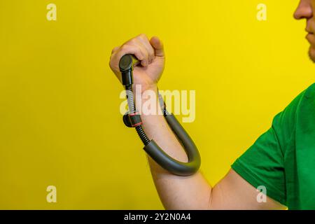 Un uomo allena i muscoli dell'avambraccio con un'impugnatura davanti a uno sfondo giallo. Foto Stock