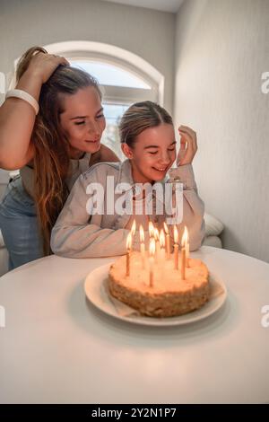 Due donne festeggiano un compleanno con una torta e candele accese. Una donna sta tenendo i capelli e sorridendo, l'altra sta soffiando via le candele. Foto Stock
