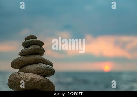 In primo piano si erge una pila di rocce accuratamente impilate, con un tramonto sull'oceano sullo sfondo. Foto Stock