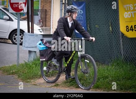 Un giovane ebreo ortodosso con abiti tradizionali si dirige fuori per fare shopping sulla sua bici e indossare un casco. Foto Stock