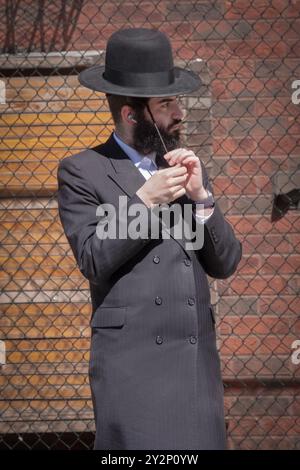 Un ebreo ortodosso gira il suo peyus e li fa ricci. Su una fermata dell'autobus a Brooklyn, New York. Foto Stock